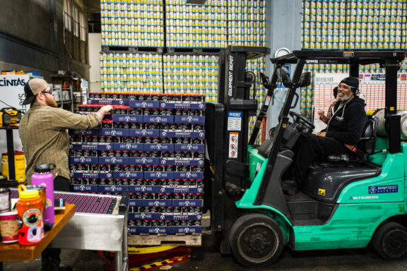 Man stacking cans and man picking up cans with forklift