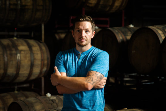 man posing with barrels in basement of Rhinegeist Brewery