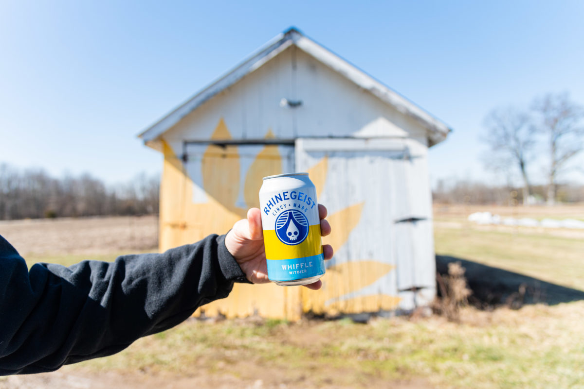 hand holding beer can in front of shed